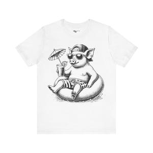May include: A white t-shirt with a black and white illustration of a pig wearing sunglasses and a hat, holding a drink and floating on a pool float. The pig is wearing swim trunks and there is an umbrella in the background.