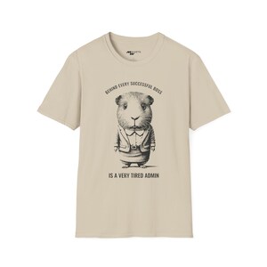 May include: A beige t-shirt featuring a black and white illustration of a guinea pig wearing a suit and tie. The text "Behind every successful boss is a very tired admin" is printed on the shirt.