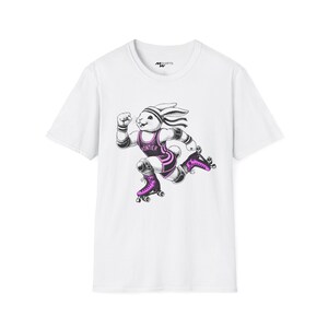 May include: White t-shirt with a graphic of a rabbit wearing a pink wrestling singlet and roller skates. The rabbit is running and has a determined expression on its face. The text "Frontier" is printed on the singlet.