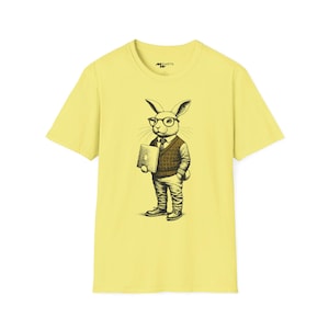 Könnte beinhalten: Ein gelbes T-Shirt mit einem Aufdruck eines Kaninchens, das eine Brille trägt und ein Buch hält. Das Kaninchen trägt eine braune Strickweste und eine Hose.