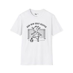 May include: White t-shirt with a black and white illustration of a goat wearing a soccer uniform and holding a soccer ball. The text "OUR NEW GOAT KEEPER" is printed above the illustration.