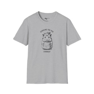 Può includere: T-shirt grigia con un grafico di un criceto che indossa un cappello da cuoco e un grembiule. Il testo "Stirring the pot literally" è stampato sotto il criceto.