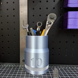 May include: A silver metal socket organizer with the number 10 printed on the side. The organizer is filled with various tools, including a wrench, screwdriver, and a few other tools.