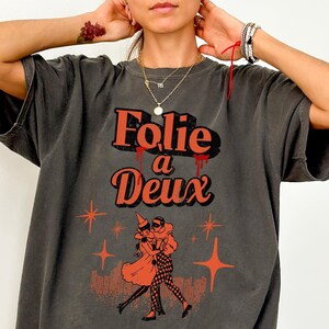 May include: A charcoal gray oversized t-shirt with a graphic print of a couple dancing. The text "Folie a Deux" is printed in orange and red.