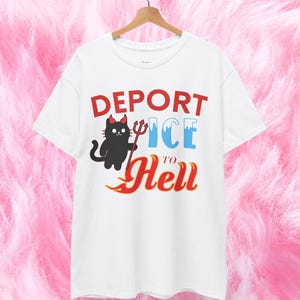 Op de afbeelding: Wit t-shirt met de tekst "DEPORT ICE to Hell" in rood en blauw. Een zwarte kat met een rode strik en een drietand-afbeelding staat op het shirt. Het woord "WHITE" staat rechtsonder gedrukt.