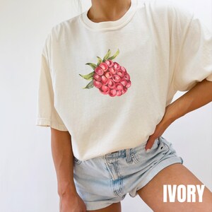 May include: A white t-shirt with a watercolor illustration of a raspberry on the front. The text "IVORY" is printed in white on a black background in the bottom right corner of the image.