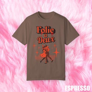 May include: A brown t-shirt with the text "Folie a Deux" in red and a vintage illustration of a couple dancing.
