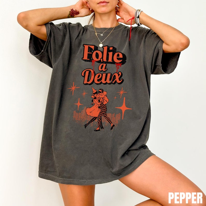 May include: A charcoal gray oversized t-shirt with a graphic print of a couple dancing. The text "Folie a Deux" is printed in orange and red.