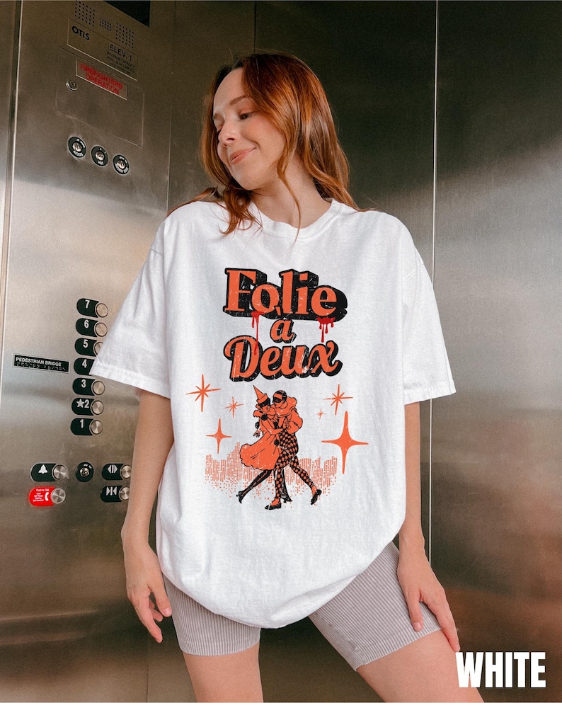 May include: White oversized t-shirt with a graphic print of a couple dancing. The graphic features the text "Folie a Deux" in red and black with dripping red paint. The background of the graphic is a black and white cityscape with stars.