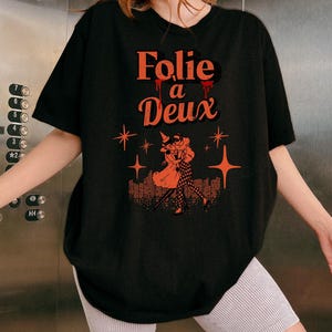 May include: Black oversized t-shirt with a graphic print of a couple dancing with the text "Folie a Deux" in red.