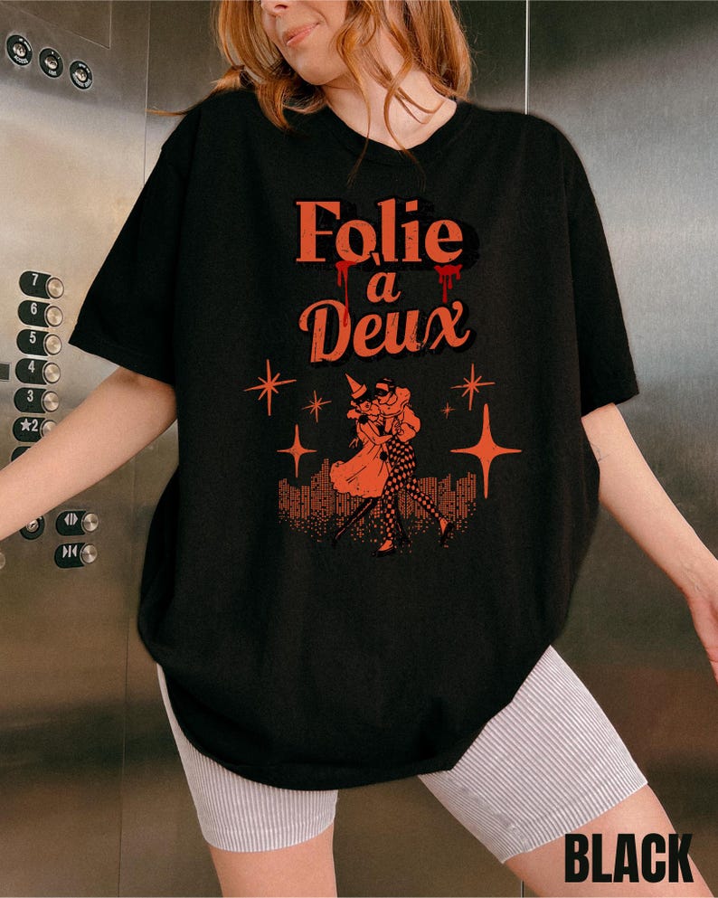 May include: Black oversized t-shirt with a graphic print of a couple dancing with the text "Folie a Deux" in red.