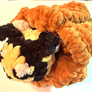 May include: A crocheted stuffed animal in the shape of a dog. The dog is brown, black, and white and is curled up in a ball. The dog is made of yarn and has a soft, fuzzy texture.