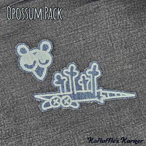May include: Two embroidered patches on a dark grey denim fabric. One patch depicts a stylised opossum head, and the other shows a long, pointed shape with four vertical tree-like structures. The text OPOSSUM PACK and Kafluffle's Korner are visible.