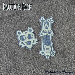 May include: Two denim fabric patches featuring raccoon designs on a dark grey heathered background. The text RACCOON PACK is printed in white at the top, and the text Ruffle's Korner is printed in black at the bottom right corner.