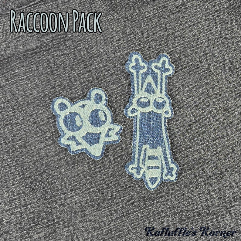 May include: Two denim fabric patches featuring raccoon designs on a dark grey heathered background. The text RACCOON PACK is printed in white at the top, and the text Ruffle's Korner is printed in black at the bottom right corner.