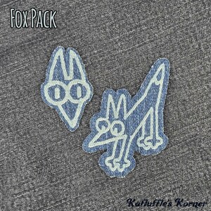 May include: Two denim fabric patches featuring white embroidered outlines of a fox head and a full-body fox. The text FOX PACK is printed in the upper left corner, and the text Kathuffle's Korner is printed in the lower right corner.