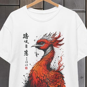 Puede incluir: Camiseta blanca con una ilustración de tinta roja y negra de un fénix con caligrafía japonesa que dice "鳳凰飛翔" (Fénix volando).