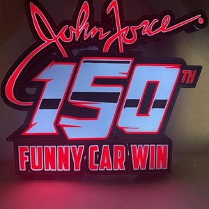 May include: A black and red sign with the text "John Force" in a cursive font. Below, the number "150" is displayed in light blue with a red outline, and the words "Funny Car Win" are at the bottom.