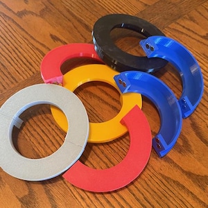 May include: A collection of colorful, circular objects in red, yellow, blue, black, and gray. The objects are arranged on a wooden surface, with some appearing to be segmented or curved. The shapes vary in thickness and design.