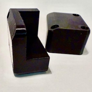 May include: Two dark brown, geometric furniture components. One is L-shaped, with a textured side. The other is a rectangular block with four holes on top. Both have a matte finish and are set against a light background.