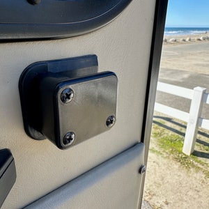 May include: A black plastic door handle with three screws visible on the side of a beige door.