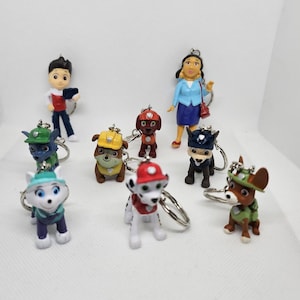 Könnte beinhalten: Eine Sammlung von Paw Patrol-Charakter-Schlüsselanhängern. Die Schlüsselanhänger zeigen verschiedene Charaktere in ihren Uniformen, darunter Marshall, Chase, Skye und Ryder. Jede Figur ist detailliert mit leuchtenden Farben und an einem silbernen Schlüsselring befestigt.