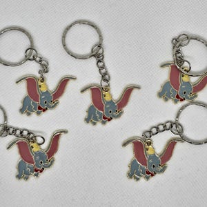 Peut inclure: Porte-clés avec un motif de l'éléphant Dumbo. Les porte-clés ont un anneau et une chaîne de couleur argentée. Les figurines de Dumbo sont grises avec des oreilles roses, un chapeau jaune et un col rouge. Les porte-clés sont en métal.