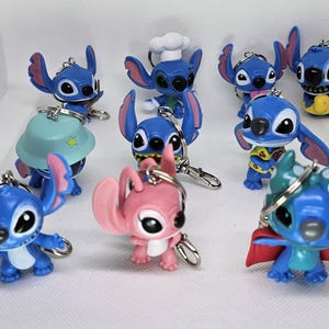 Könnte beinhalten: Eine Sammlung von zehn blauen Stitch- und Angel-Schlüsselanhängern. Die Schlüsselanhänger zeigen verschiedene Designs, darunter Stitch mit einem Kochhut, Stitch mit einem Hawaiihemd, Stitch mit einem Superhelden-Umhang und Angel mit einem rosa Kleid.
