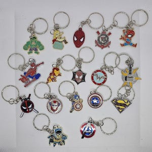 Può includere: Collezione di portachiavi in metallo con vari personaggi di fumetti e supereroi. I portachiavi includono Hulk, Spider-Man, Iron Man, Captain America e loghi di Superman, con portachiavi argentati.