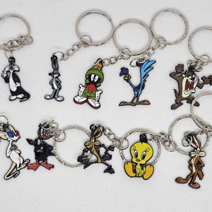 Peut inclure: Une collection de porte-clés de personnages de dessins animés. Les porte-clés présentent des personnages tels que Sylvestre le Chat, Bugs Bunny, Marvin le Martien, Bip Bip, Taz, Pinky et Titi. Chaque porte-clés a un anneau argenté.