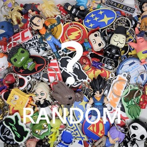 May include: A jumble of keyrings with various designs, including cartoon characters and logos. The word "RANDOM" is written in white. Keyrings feature characters like the Hulk, SpongeBob, and figures from Dragon Ball Z.