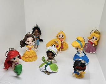 Puede incluir: Un conjunto de ocho dijes de princesa Disney para llavero. Los dijes están hechos de plástico y presentan diferentes princesas, incluyendo Ariel, Bella, Cenicienta, Blancanieves, Tiana, Jasmine, Rapunzel y Aurora. Los dijes están todos en un estilo chibi, con cabezas grandes y cuerpos pequeños.