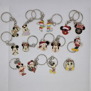 Könnte beinhalten: Sammlung von Disney-Charakter-Schlüsselanhängern. Enthält Designs von Mickey Mouse, Minnie Mouse und Snoopy. Einige Schlüsselanhänger zeigen Urlaubsthemen mit Weihnachtsmützen. Jeder Schlüsselanhänger hat einen silbernen Metallring.