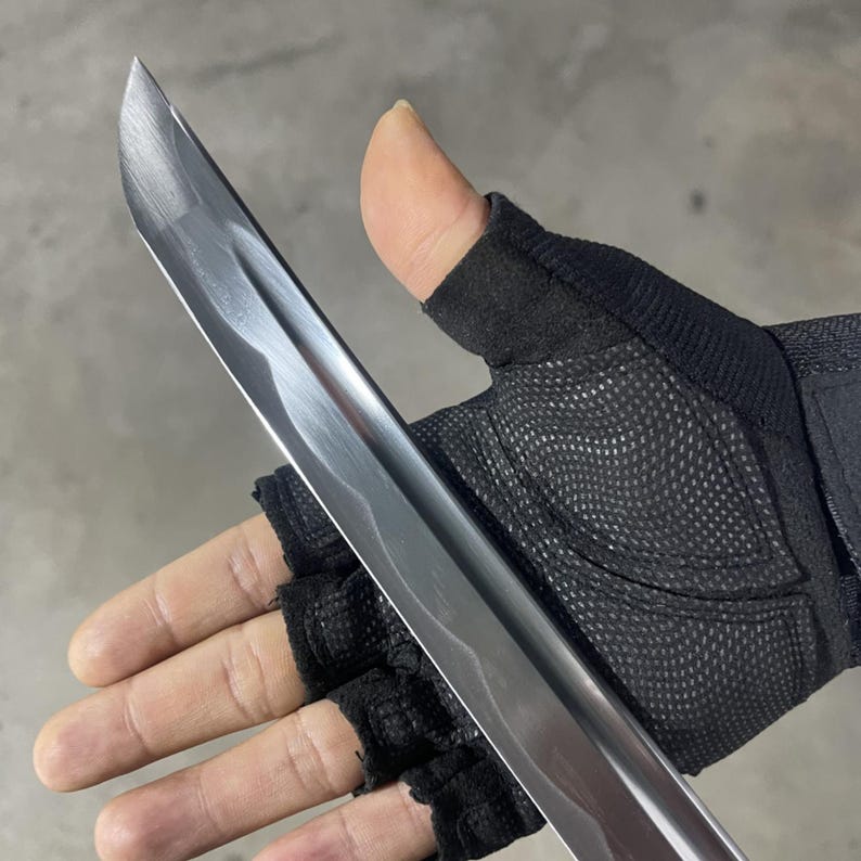 May include: A silver-coloured katana sword with a slightly curved blade. The sword is held in a gloved hand.