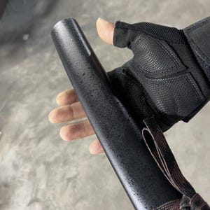 May include: A black, textured, cylindrical object with a brown strap. The object is being held by a hand wearing a black fingerless glove.