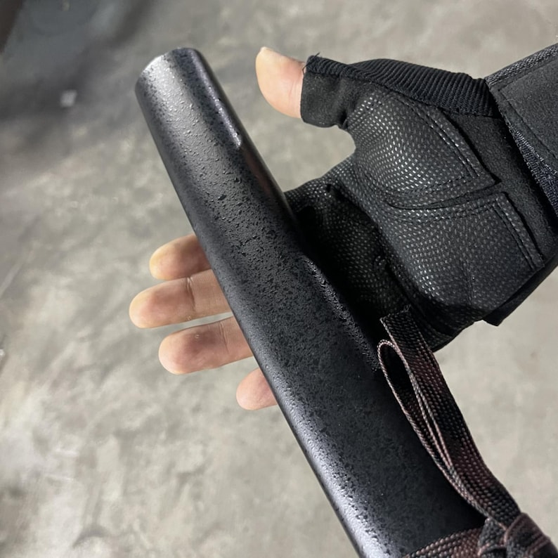 May include: A black, textured, cylindrical object with a brown strap. The object is being held by a hand wearing a black fingerless glove.