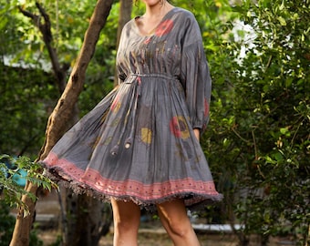 May include: A gray, floral print dress with a cinched waist and a ruffled hem. The dress has a V-neckline and long sleeves. The model is wearing the dress in a garden setting.