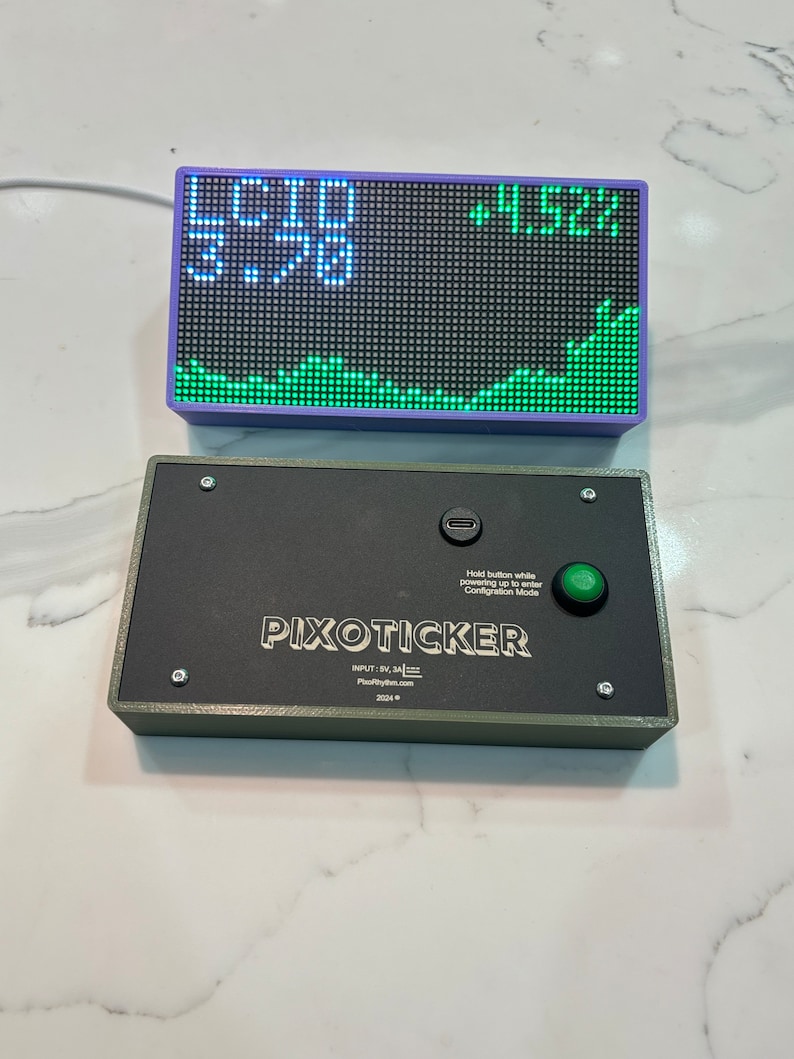 May include: A digital stock ticker with a purple frame displays numbers and a green line graph. Below it, a black box with the text "PIXOTICKER" and a green button is visible. The text "Hold button while powering up to enter Configuration Mode" is also present.
