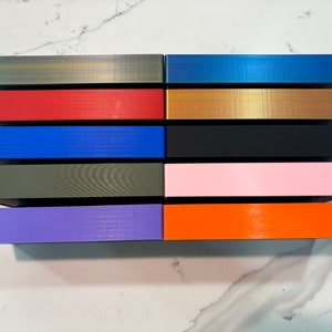 May include: A collection of rectangular boxes in various colors, including gold, red, blue, black, pink, and orange. The boxes have a textured surface and are arranged in rows. The color palette is diverse, offering a range of options.