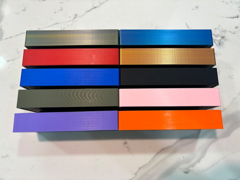 May include: A collection of rectangular boxes in various colors, including gold, red, blue, black, pink, and orange. The boxes have a textured surface and are arranged in rows. The color palette is diverse, offering a range of options.