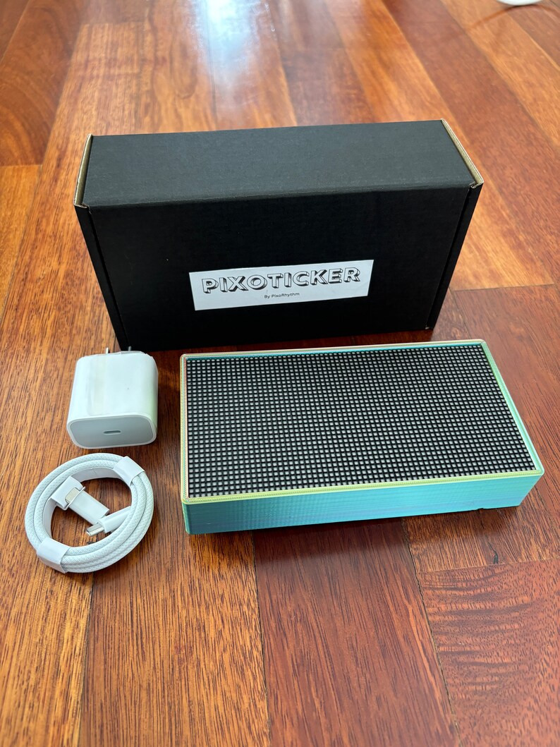 May include: A mint green and black speaker with a black box, charger, and white cable. The speaker has a grid pattern on the front. The box is black with the text "PIXOTICKER" in white. The charger is white.