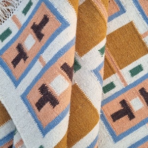 May include: A white, blue, green, and brown woven rug with a geometric pattern. The rug is folded in half, showing the pattern on both sides.