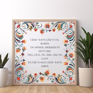 Könnte beinhalten: Ein weißer gerahmter Druck mit einem bunten floralen Rand. Der Druck zeigt ein traditionelles skandinavisches Volkskunstdesign mit weißem Hintergrund und einem Text in Rot und Blau, der lautet: "I JESU NAVN GÅR VI TIL BORDS OG SPISER, DRIKKER PÅ DITT ORD DEG, GUD, TIL ÆRE, OSS TIL GAVN SÅ FÅR VI MAT I JESU NAVN. AMEN."