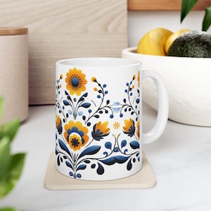 May include: White ceramic mug with a floral design featuring blue and yellow flowers on a white background. The mug has a white handle.