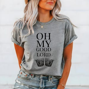 May include: Grey t-shirt with the text "OH MY GOOD LORD" and two black and white illustrations of glasses of alcohol.