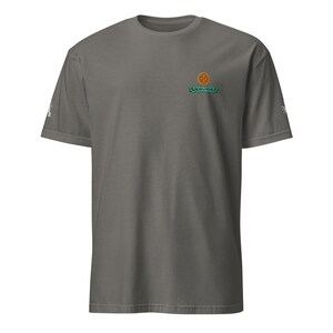 May include: A charcoal gray t-shirt with a small embroidered logo on the left chest. The logo is a green and orange design with a circle in the center.