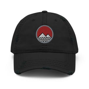 Puede incluir: Gorra de béisbol negra desgastada con una escena de montaña bordada en rojo y blanco dentro de un círculo.