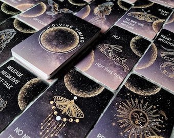 May include: A deck of oracle cards with celestial and nature-inspired illustrations. The cards feature phrases like "Divine Timing," "No Need to Worry," and "Not This Time." The color palette includes deep purples, gold accents, and a starry night sky theme.