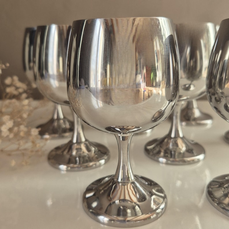 Puede incluir: Conjunto de seis copas de vino plateadas con una copa redonda y un tallo alto. Las copas est&aacute;n pulidas y reflejan la luz.