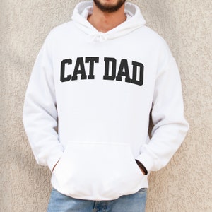 White colored pullover hoodie with Cat Dad printed in an arch on the front in black.  Varsity athletic block style font printed on the hooded sweatshirt.